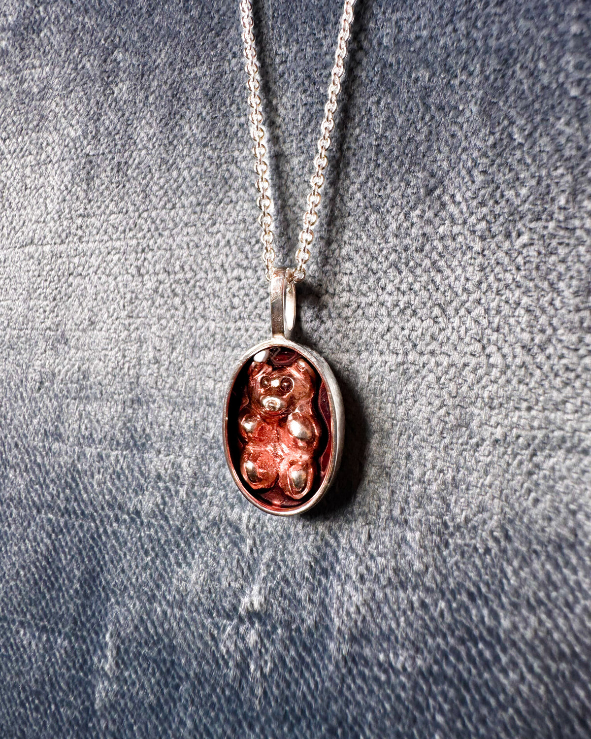 Silver pendant with pink enamel teddy bear design on a velvet background
