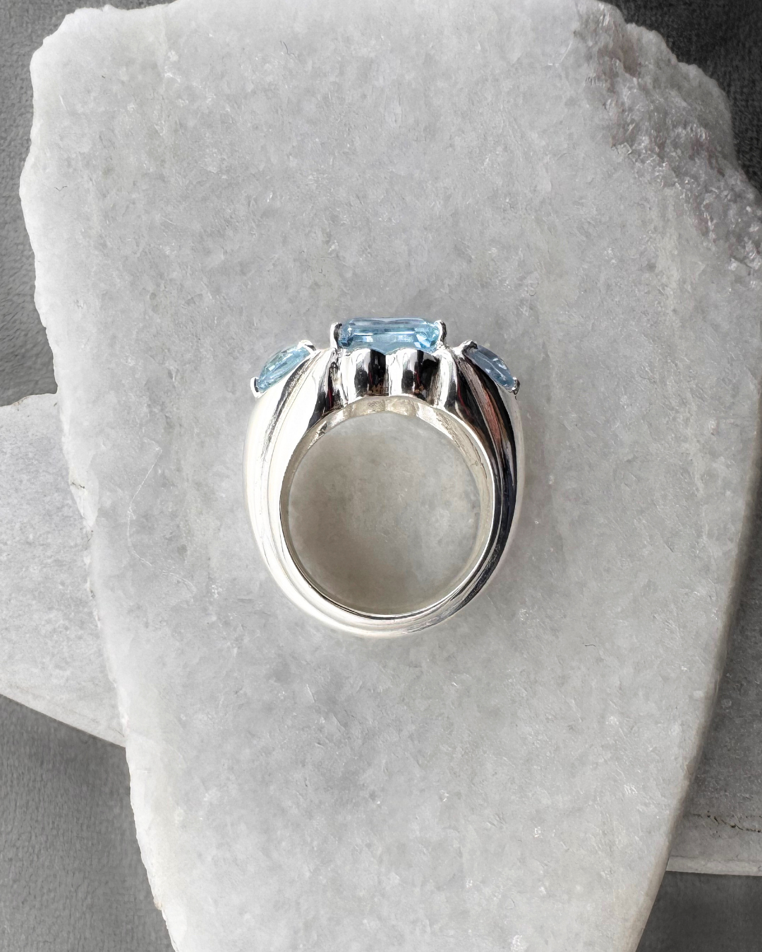 Silver ring with blue topaz gemstones on a stone surface