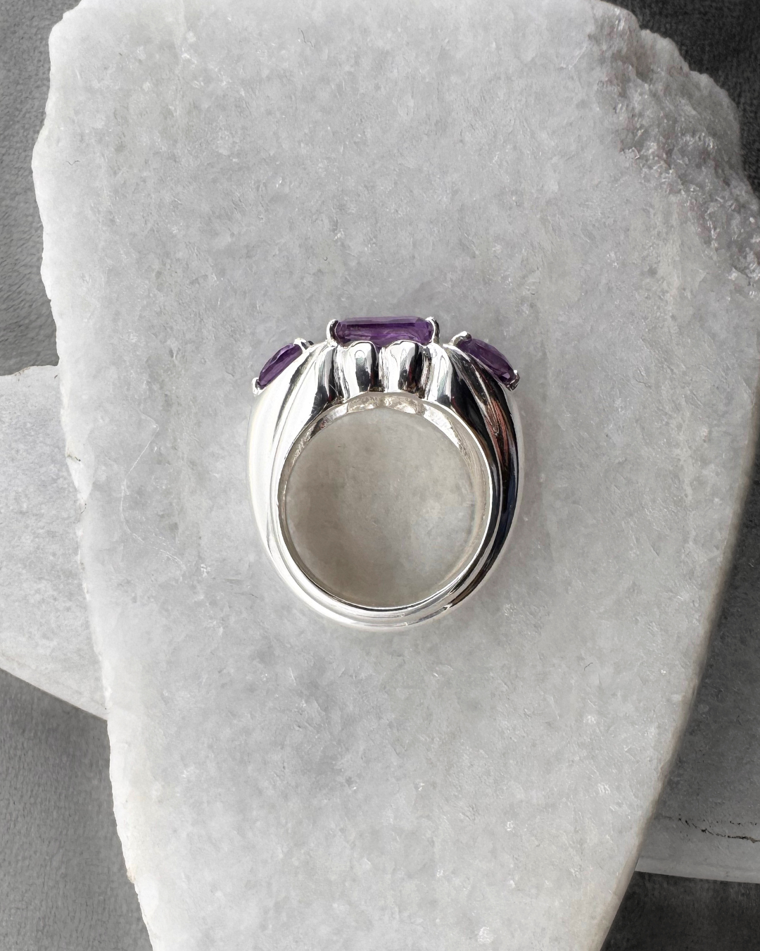 Silver ring with purple amethyst gemstones on a stone surface