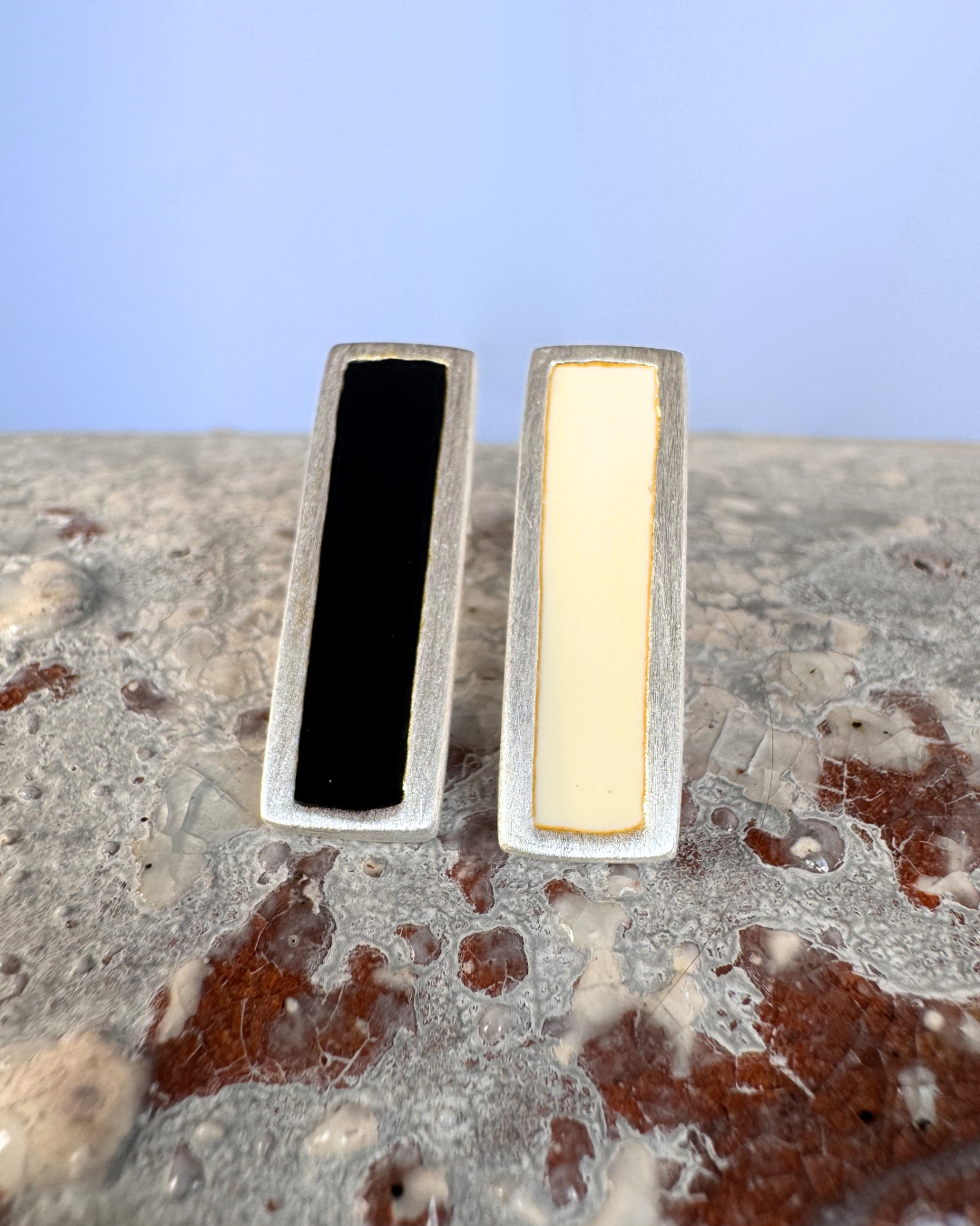 Silver stud earrings with white and black enamel bars, on stone surface