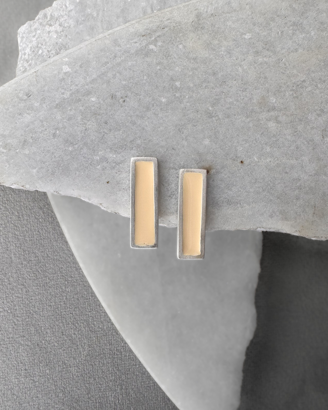 Silver stud earrings with white enamel bars, on stone surface