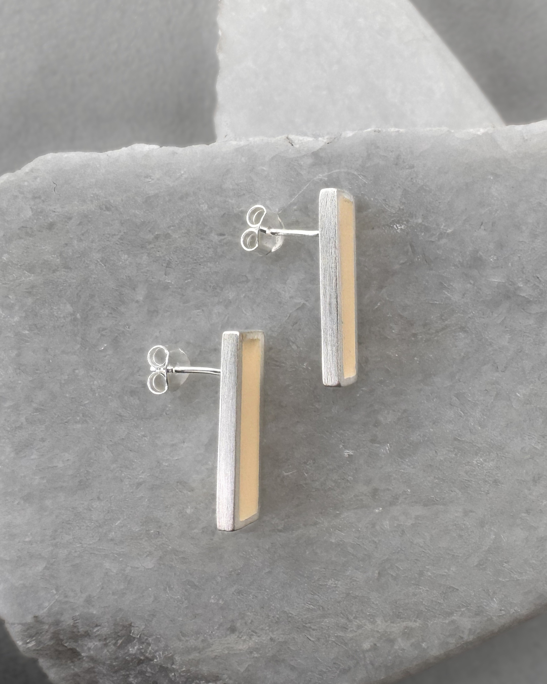 Silver stud earrings with white enamel bars, on stone surface
