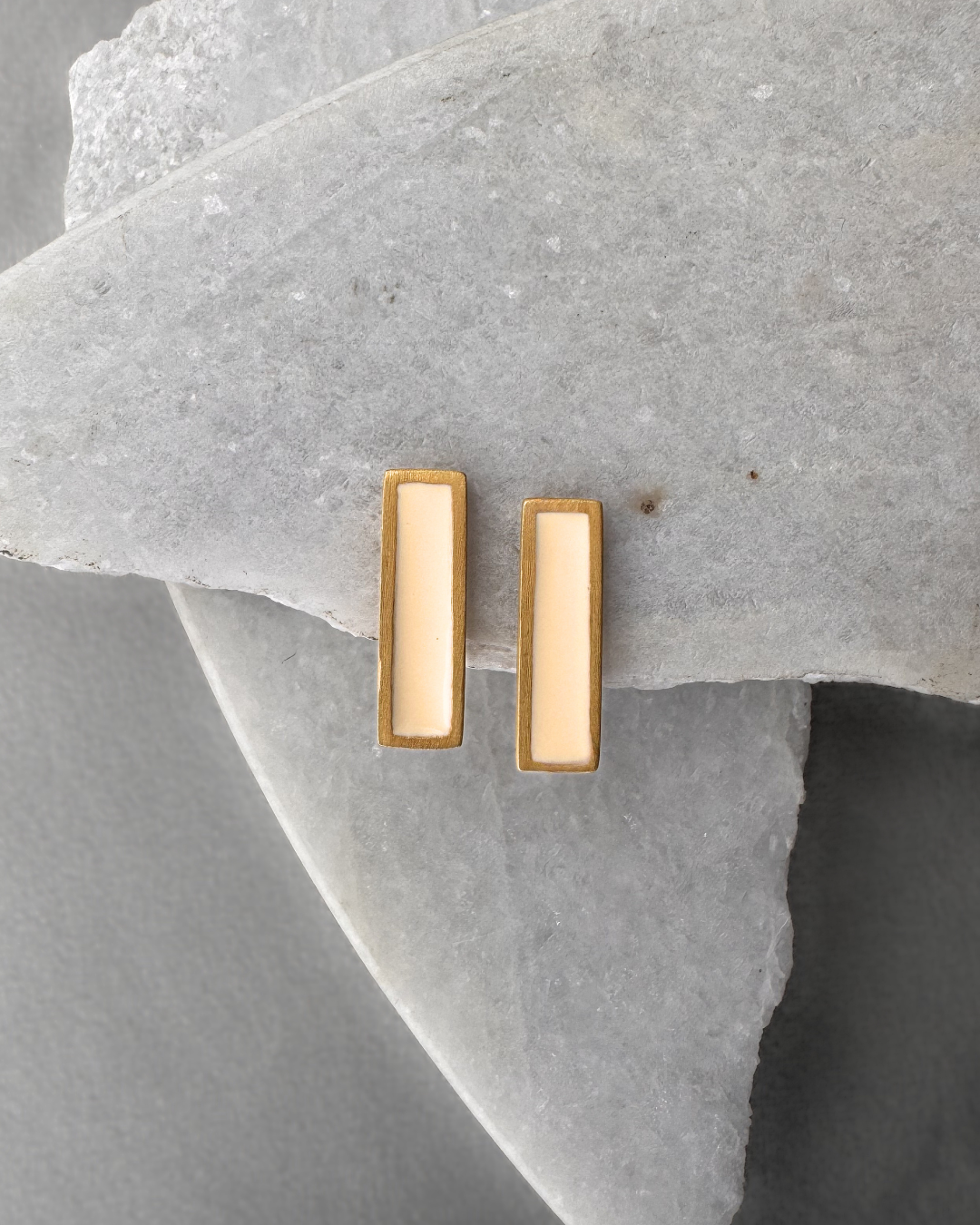 Gold-plated stud earrings with white enamel bars, on stone surface