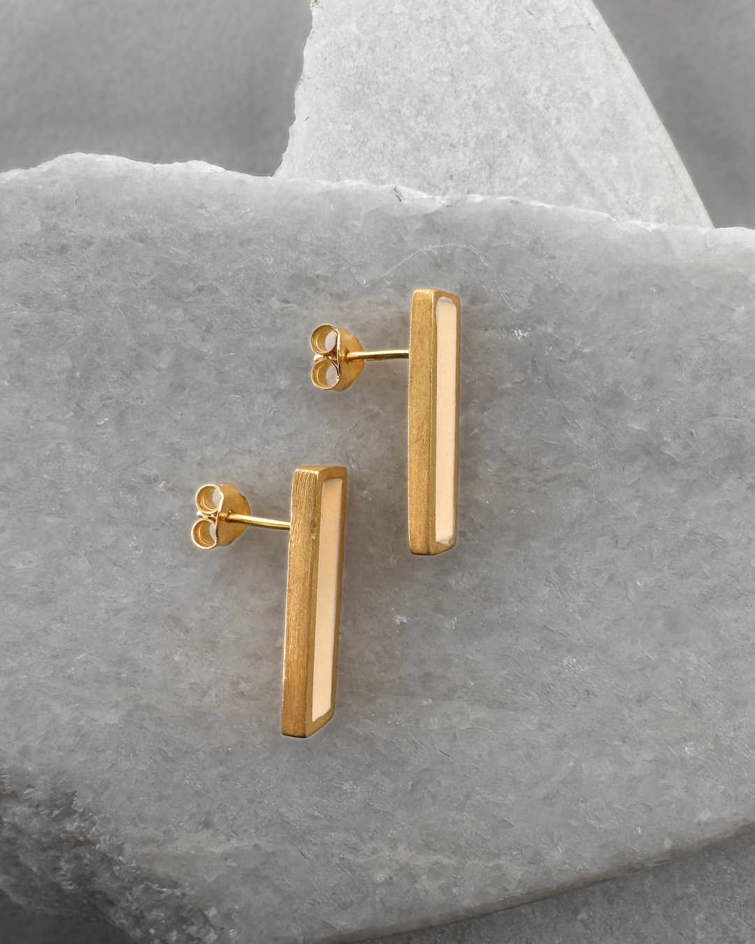 Gold-plated stud earrings with white enamel bars, on stone surface