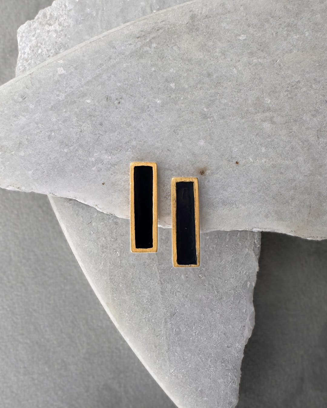Gold-plated stud earrings with black enamel bars, on stone surface