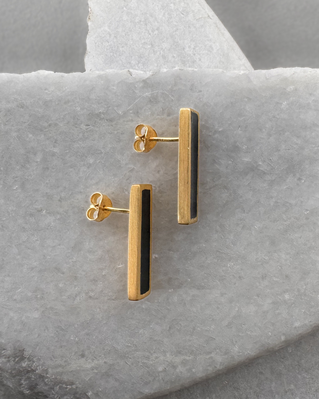 Gold-plated stud earrings with black enamel bars, on stone surface