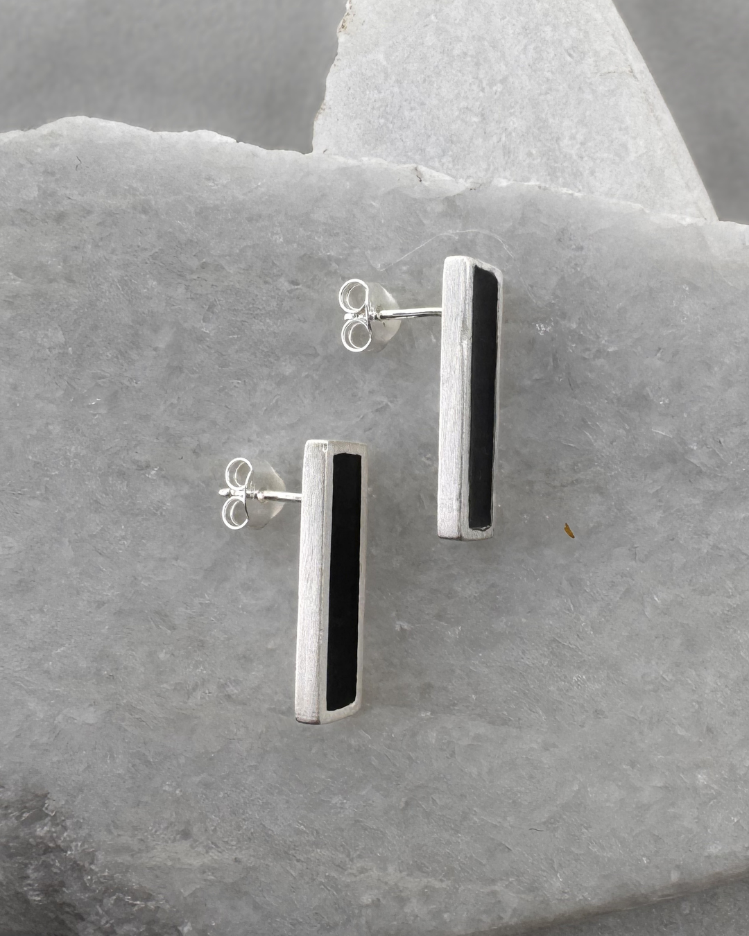 Silver stud earrings with black enamel bars, on stone surface