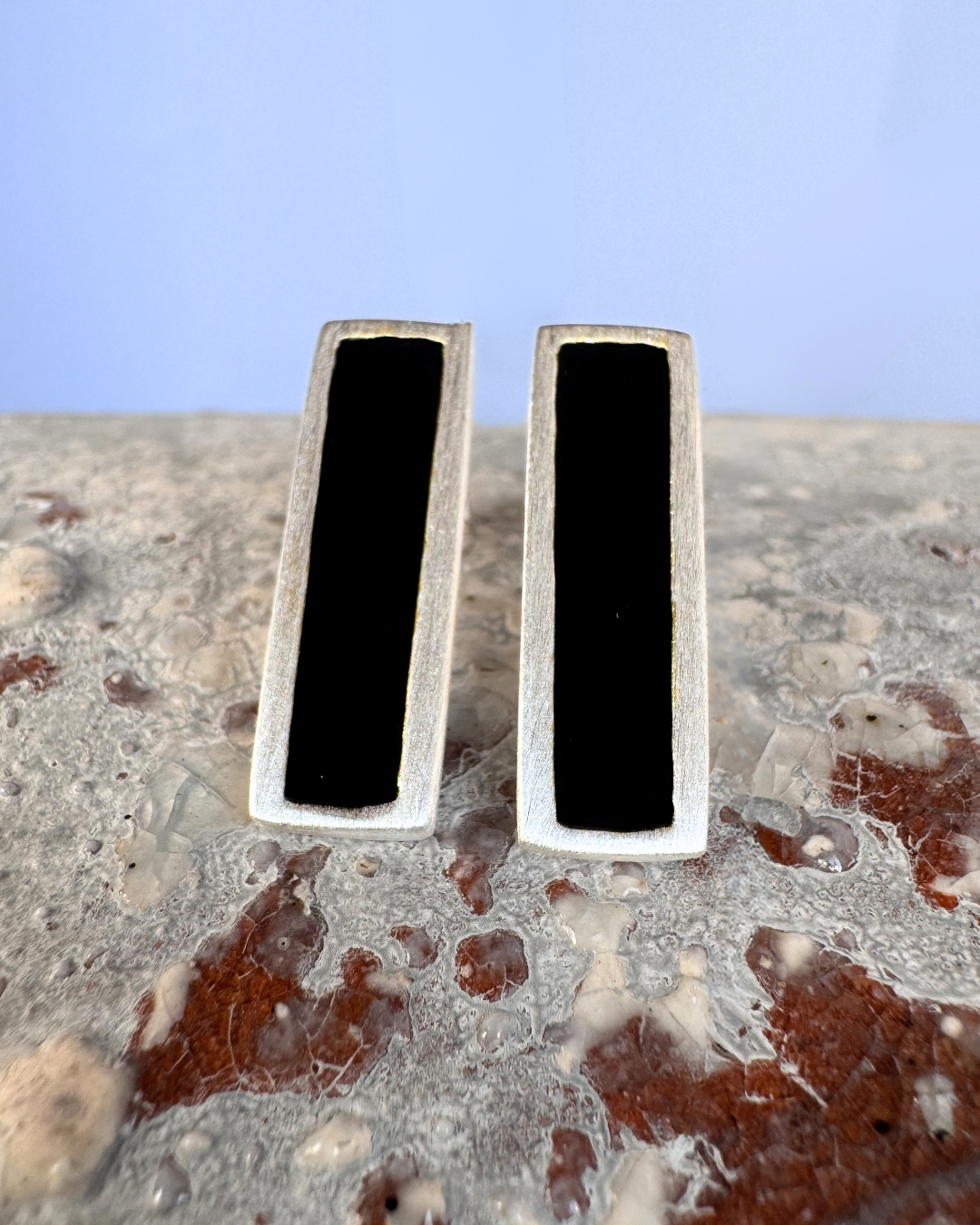 Silver stud earrings with black enamel bars, on stone surface