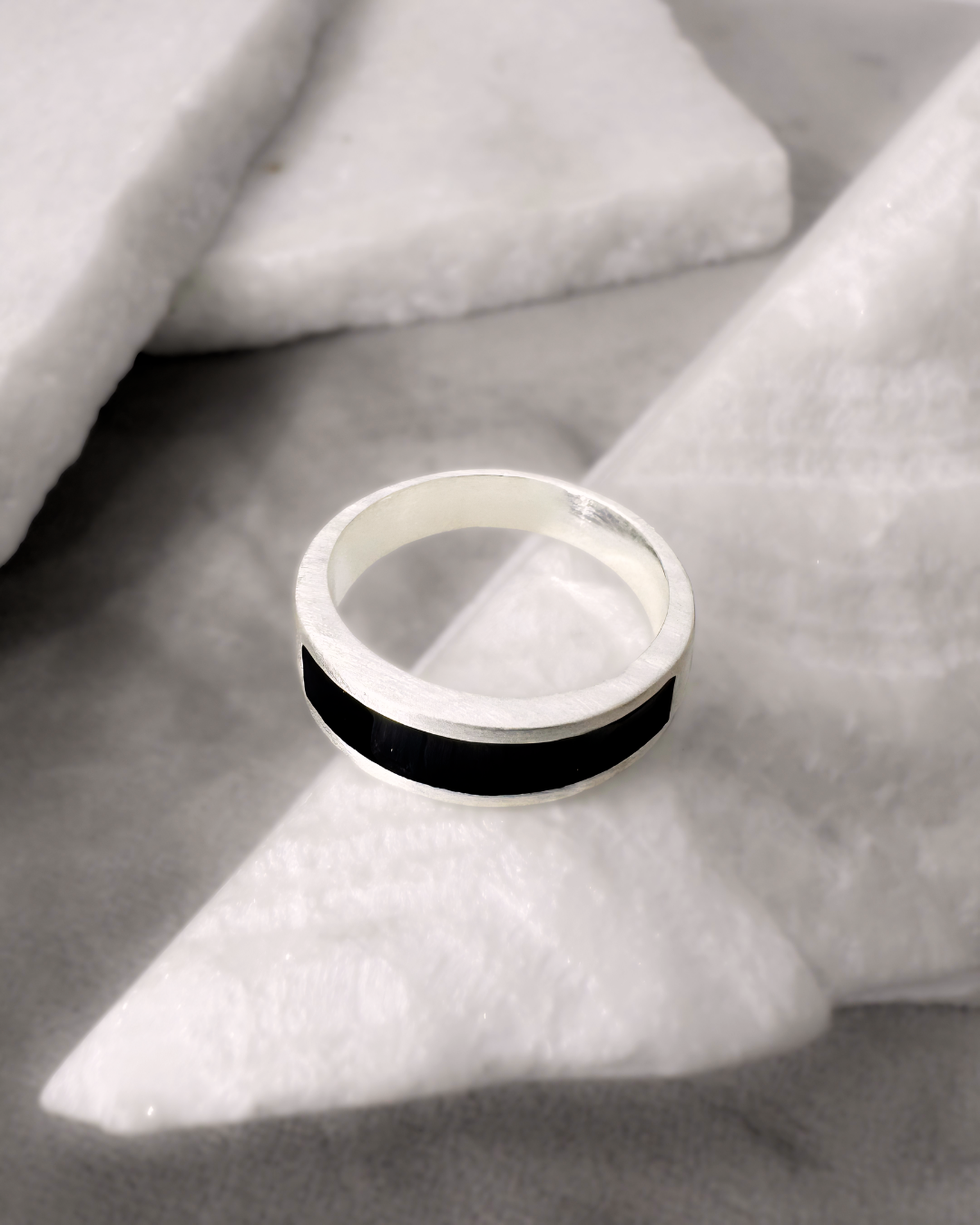Silver ring with a black enamel band on a stone background