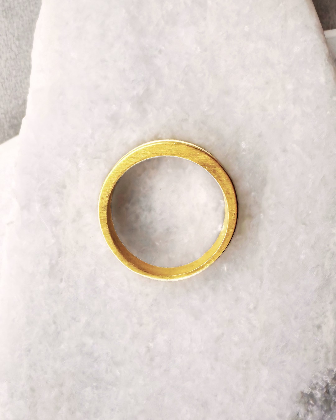 Close-up of a gold-plated ring with a white enamel band on a stone background