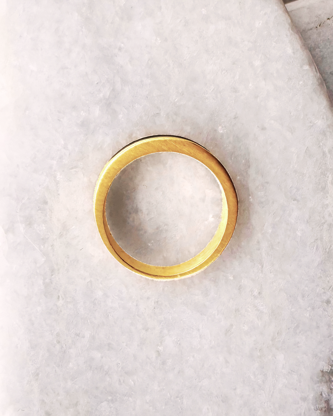 Close-up of a gold-plated ring with a white enamel band on a stone background