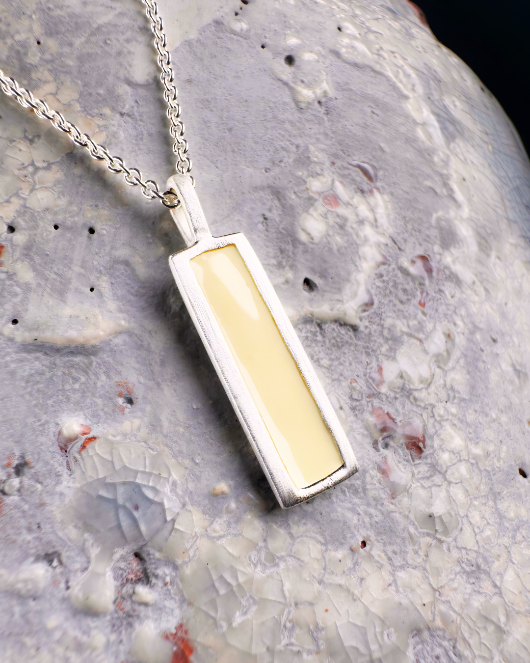 Silver pendant with rectangular white enamel, displayed on a stone surface