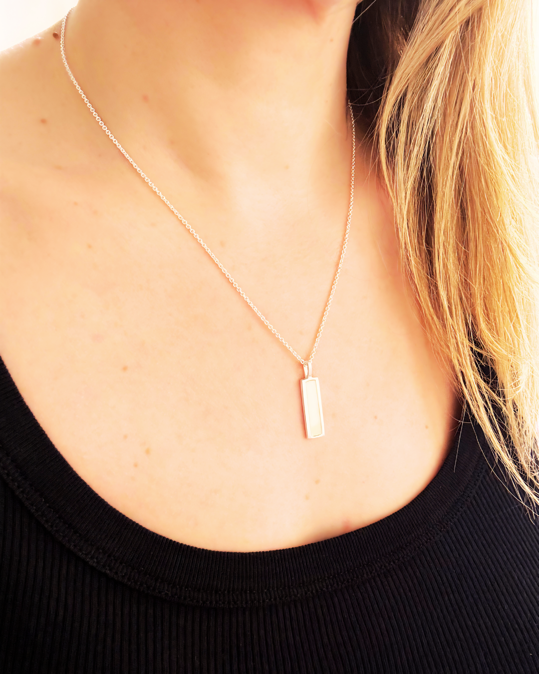 Silver pendant with rectangular white enamel, worn by a woman with a black shirt
