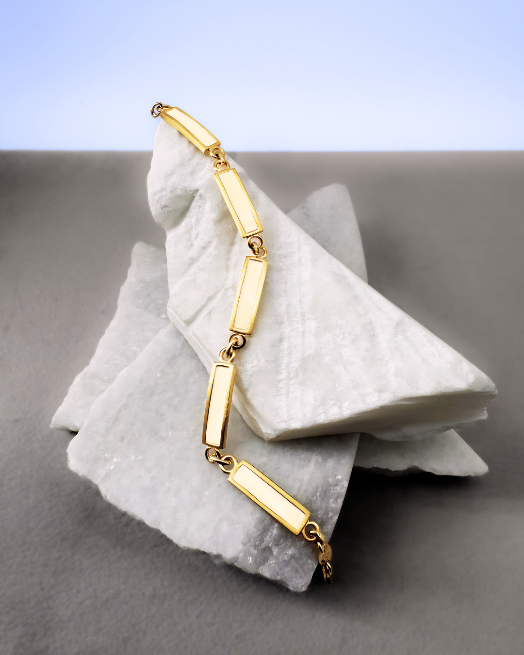 Gold-plated chain bracelet with white enamel bar links, displayed on marble stones
