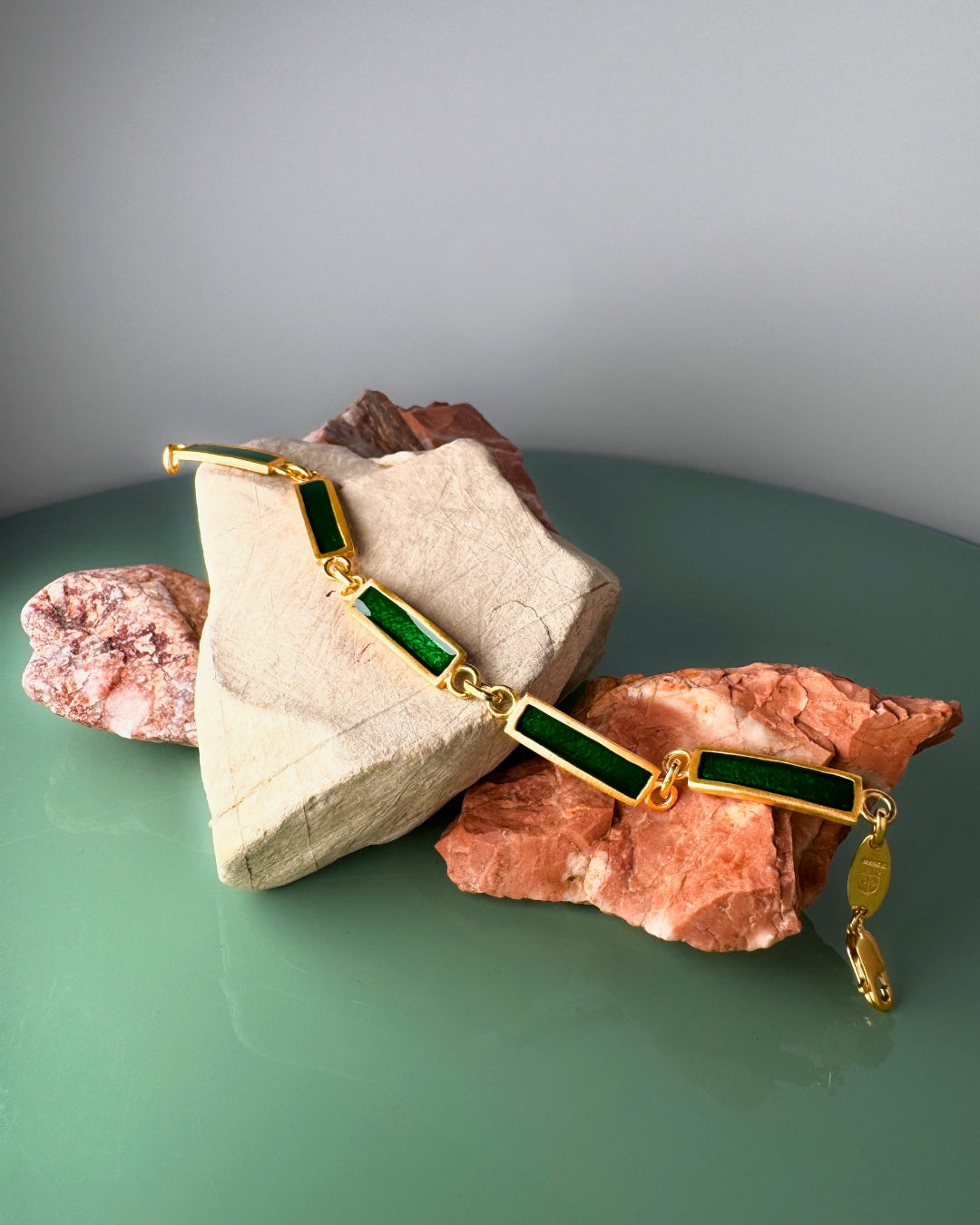 Gold-plated bracelet with rectangular green enamel links, displayed on marble stones