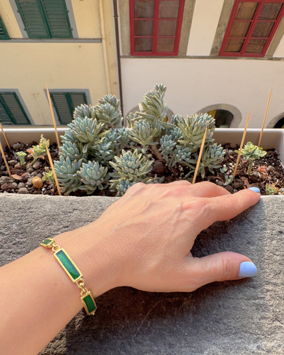 Gold plated bracelet with rectangular green enamel links on a wrist with a blurred outdoor background