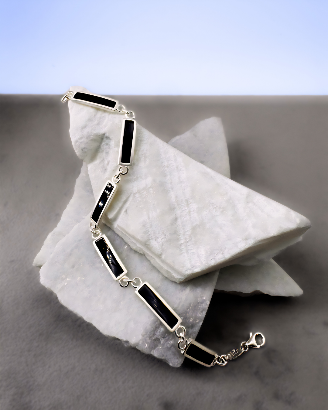 Silver chain bracelet with black enamel bar links, displayed on marble stones