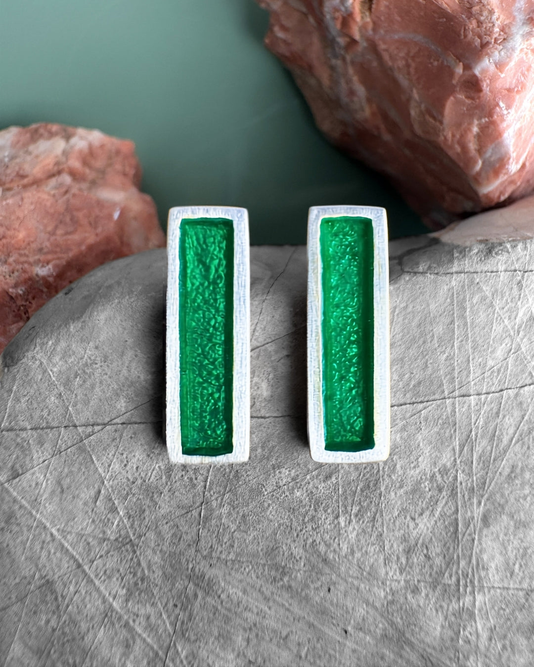 Silver stud earrings with green enamel bars, on stone surface