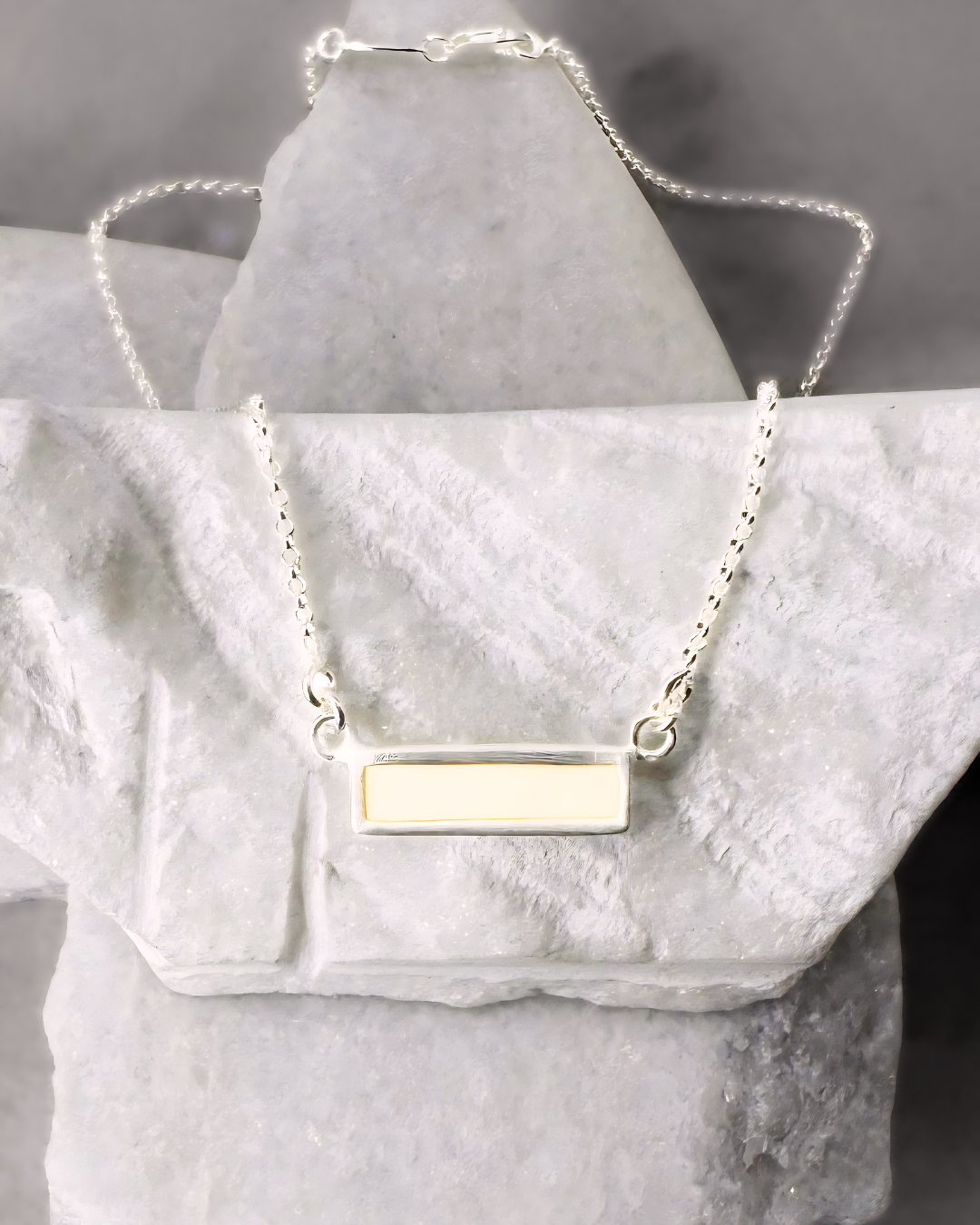 Silver necklace with rectangular white enamel, displayed on marble stones
