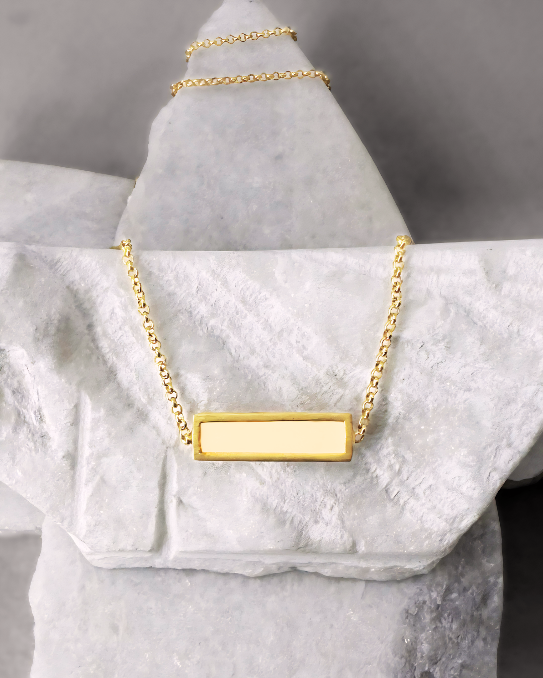 Gold plated necklace with rectangular white enamel, displayed on marble stones