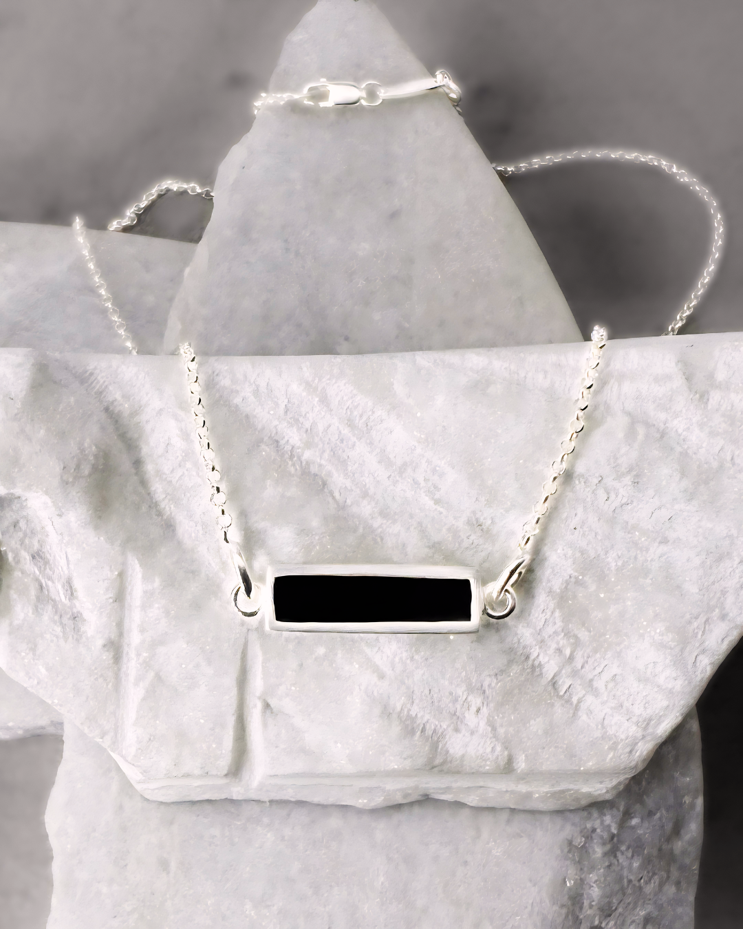 Silver necklace with rectangular black enamel, displayed on marble stones