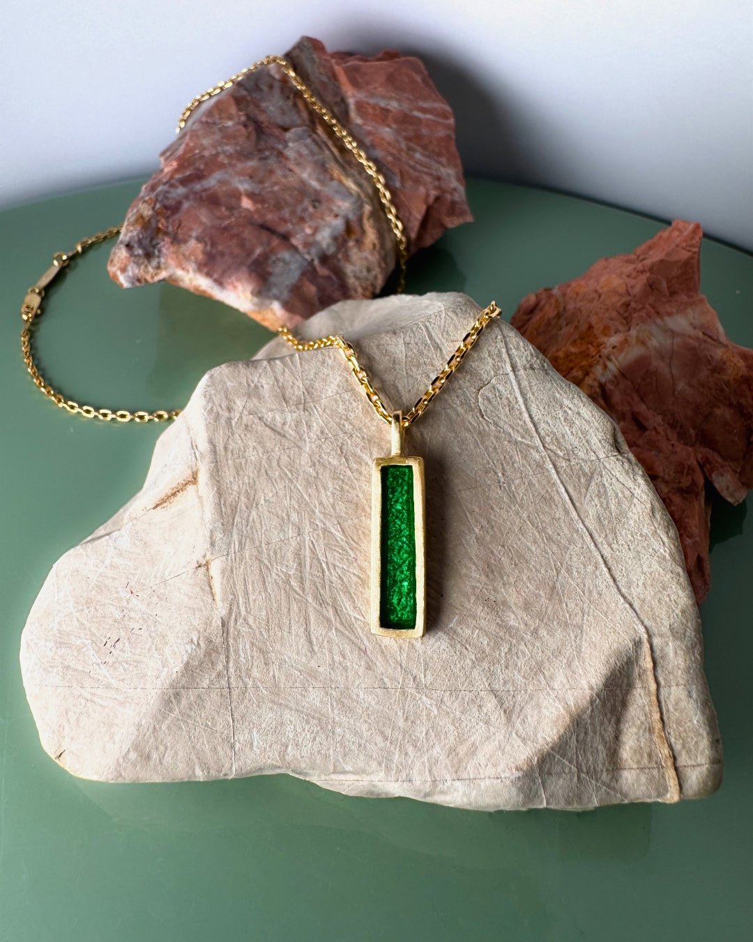 Gold plated pendant with rectangular green enamel, displayed on marble stones