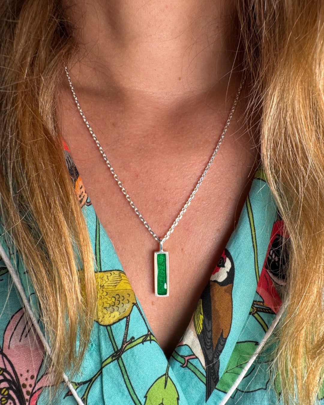 Silver pendant with rectangular green enamel, worn by a woman with a floral shirt