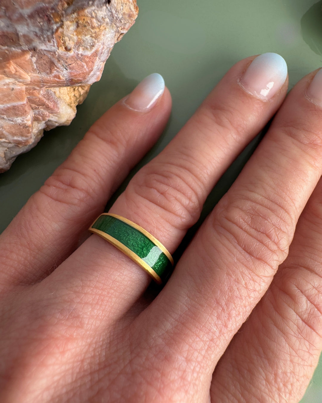 Gold-plated ring with a green enamel band, worn on a finger